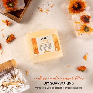 Op de afbeelding: Een transparante, rechthoekige blok van smelt- en gietzeepbasis met een label met de tekst "PIFITO Honey Melt & Pour Soap Base". De zeepbasis ligt op een wit oppervlak met verspreide gedroogde bloemen. De tekst "endless creative possibilities DIY SOAP MAKING Works great with all colorants and essential oils" staat onder de zeepbasis.