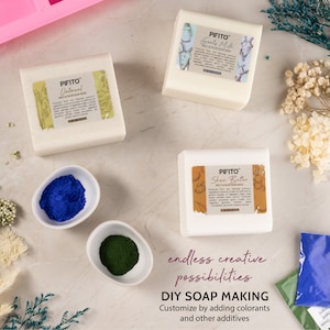 May include: An overhead shot features DIY soap-making supplies. There are three white soap base blocks labeled "Oatmeal", "Goats Milk", and "Shea Butter". Two small white bowls contain blue and green colorants. The text reads "endless creative possibilities" and "DIY SOAP MAKING".