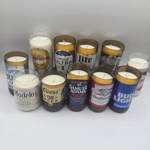 May include: A collection of beer can candles, each with a different brand label, including Bud Light, Coors, and Modelo. The candles are filled with white wax and have a single wick. The labels are in various colors.