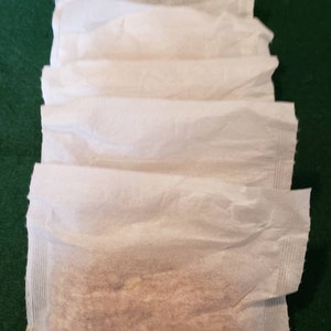 May include: Five white paper packets, four are empty and one is filled with a light brown substance.