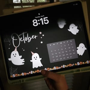 Puede incluir: Una pantalla de tableta muestra un fondo de pantalla con temática de Halloween. El fondo negro presenta fantasmas blancos, telarañas, estrellas y la palabra "October". Un calendario muestra el mes de octubre. La hora es 8:15.