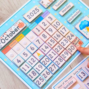 May include: A blue and white magnetic calendar with the month of October and the year 2025. The calendar has a storm weather icon and a birthday cake icon. The calendar also has a section for days of the week and extra tiles.
