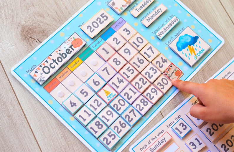 May include: A blue and white magnetic calendar with the month of October and the year 2025. The calendar has a storm weather icon and a birthday cake icon. The calendar also has a section for days of the week and extra tiles.