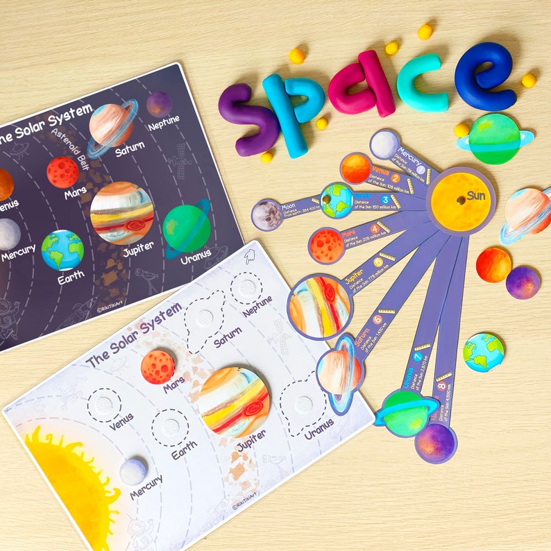Puede incluir: Dos tablas educativas coloridas sobre el sistema solar con los planetas y sus nombres. Las tablas est&aacute;n sobre una superficie de madera con letras de plastilina de colores que deletrean la palabra "espacio".