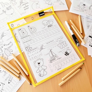 Peut inclure: Un tableau d'&eacute;criture transparent avec un cadre jaune, contenant une feuille avec la lettre "B" et des exercices de tra&ccedil;age. Comprend un marqueur effa&ccedil;able et plusieurs crayons. D'autres feuilles avec des illustrations d'animaux et des exercices d'&eacute;criture sont visibles.