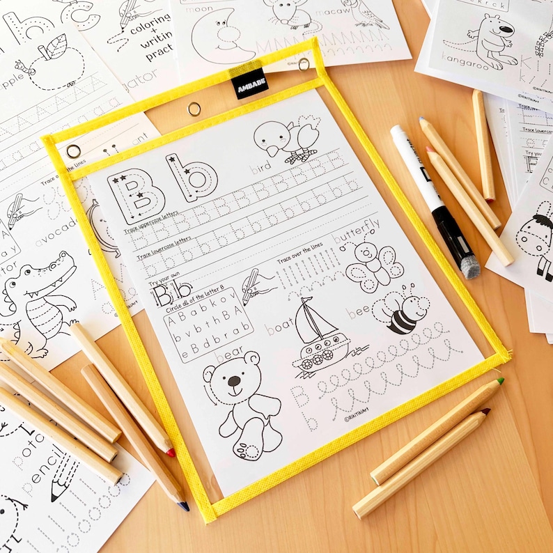 Peut inclure: Un tableau d'&eacute;criture transparent avec un cadre jaune, contenant une feuille avec la lettre "B" et des exercices de tra&ccedil;age. Comprend un marqueur effa&ccedil;able et plusieurs crayons. D'autres feuilles avec des illustrations d'animaux et des exercices d'&eacute;criture sont visibles.