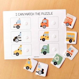 May include: A white wooden puzzle board with the text "I CAN MATCH THE PUZZLE" and illustrations of various vehicles. Includes matching puzzle pieces of a fire truck, school bus, ambulance, and more.