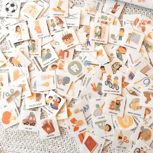 May include: A collection of small, square cards with various illustrations and text. The cards depict activities like soccer, ballet, and cycling, along with words such as "vacation" and "birthday." The cards are scattered on a textured surface.