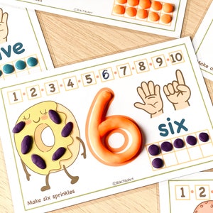 May include: A printable learning activity for kids to practice counting to six. The activity features a donut with sprinkles, a number six, and a hand with six fingers. The words "Make six sprinkles" and "six" are written on the page.