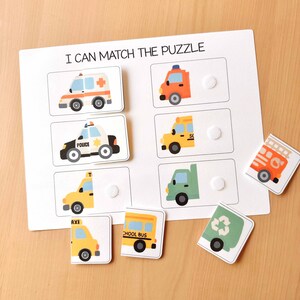 May include: A white puzzle board with the text "I CAN MATCH THE PUZZLE" features vehicle illustrations. Includes an ambulance, police car, taxi, school bus, fire truck, truck, and recycling truck. The puzzle pieces are removable.