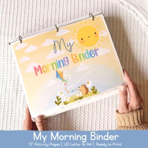 Könnte beinhalten: Ein Ordner mit einem farbenfrohen Cover mit dem Text "My Morning Binder". Das Cover-Design zeigt eine lächelnde Sonne, Wolken, einen Drachen und einen Igel. Der Ordner ist geöffnet und zeigt die Seiten im Inneren. Der Text "My Morning Binder" steht ebenfalls unten.