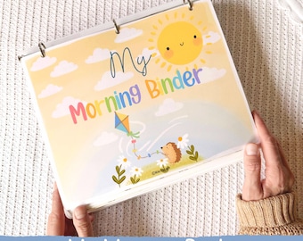 May include: A binder with a colorful cover featuring the text "My Morning Binder". The cover art includes a smiling sun, clouds, a kite, and a hedgehog. The binder is held open, revealing the pages inside. The text "My Morning Binder" is also at the bottom.