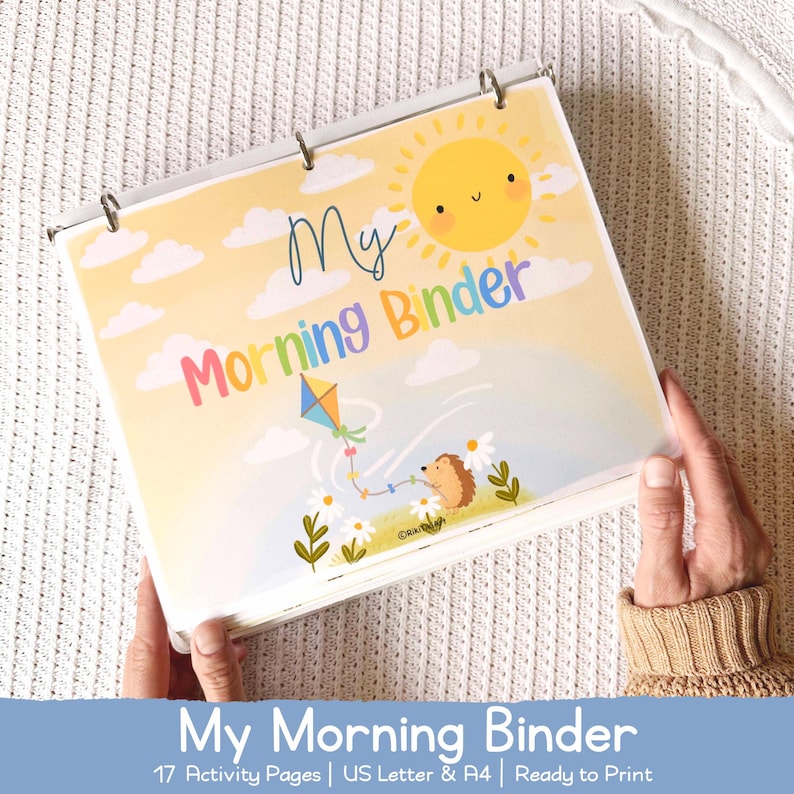 May include: A binder with a colorful cover featuring the text "My Morning Binder". The cover art includes a smiling sun, clouds, a kite, and a hedgehog. The binder is held open, revealing the pages inside. The text "My Morning Binder" is also at the bottom.