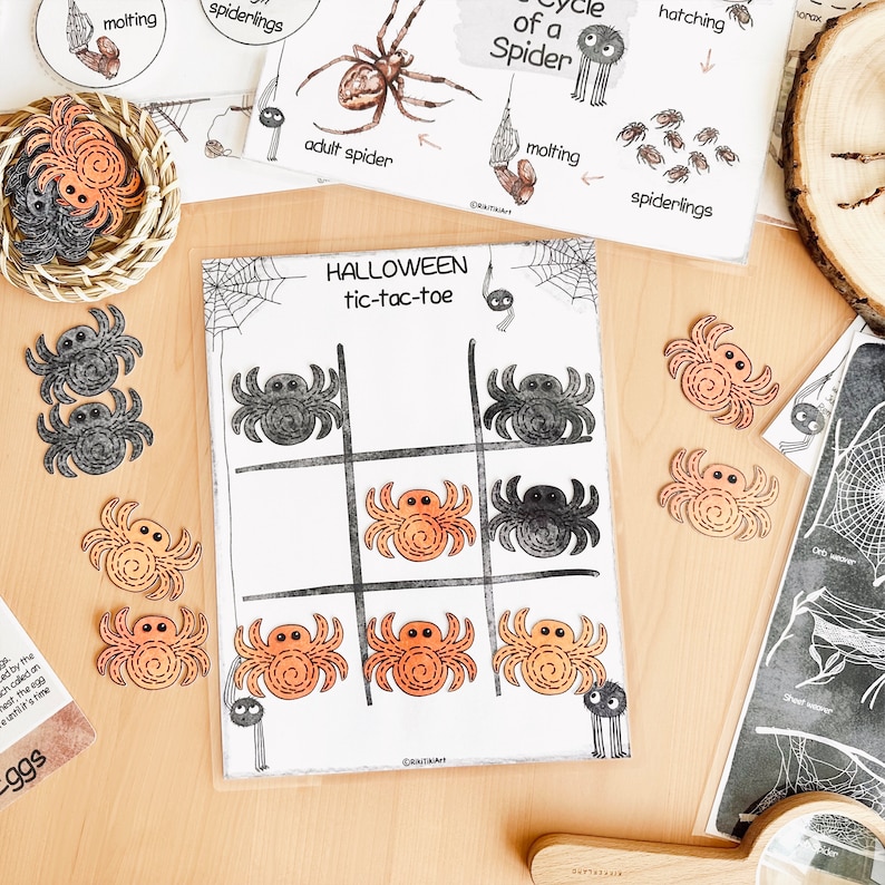 May include: A Halloween-themed tic-tac-toe game with a spider web design. The game board has nine squares, and each square has a black or orange spider. The game is played with two sets of spider tokens, one black and one orange.