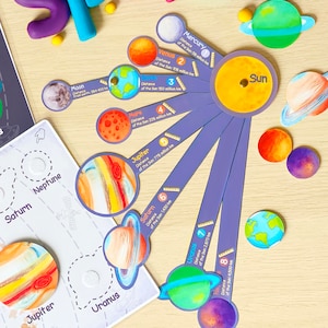 Puede incluir: Un juguete educativo colorido que representa los planetas de nuestro sistema solar. Cada planeta est&aacute; representado por una tarjeta circular con una ilustraci&oacute;n y el nombre del planeta. Las tarjetas est&aacute;n dispuestas en un patr&oacute;n radial alrededor de una tarjeta central del sol, con la distancia del sol indicada en cada tarjeta.