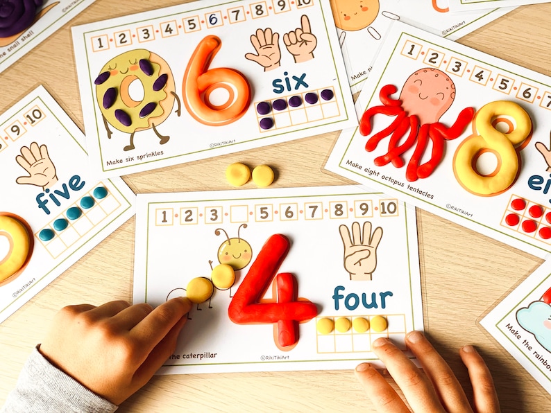 May include: A set of printable learning cards for kids featuring colorful play dough numbers and counting activities. The cards include a donut with sprinkles, an octopus with tentacles, a caterpillar, and a hand with fingers. The text on the cards includes the numbers 1 through 10, the words "six", "five", "four", and instructions to "Make six sprinkles", "Make eight octopus tentacles", and "Make the rainbow".