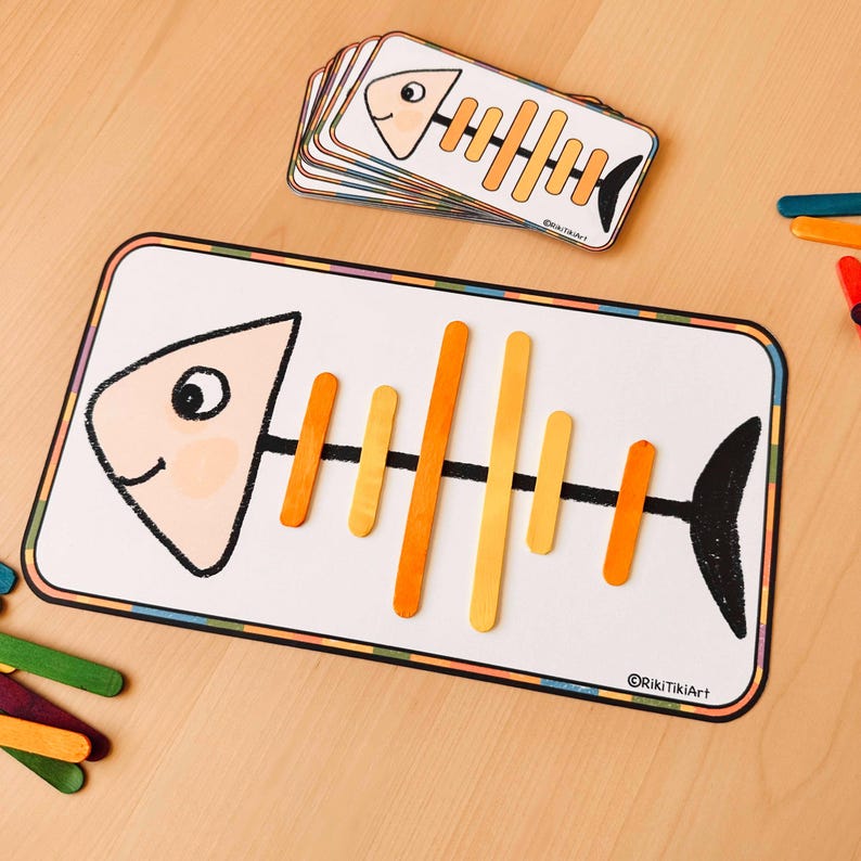 May include: A printable fish skeleton template with a fish outline and a set of orange and yellow craft sticks to create the skeleton. The template has a white background with a black outline and a colourful border. The text "@RikitkiArt" is in the bottom right corner.