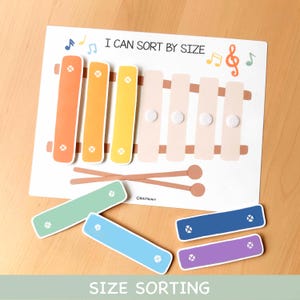 Puede incluir: Un juguete educativo con diseño de xilófono y el texto "I CAN SORT BY SIZE" y "SIZE SORTING". El juguete presenta un diseño de xilófono con barras de varios colores y piezas de clasificación adicionales en verde, azul y morado.