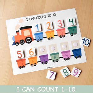Puede incluir: Un colorido tablero educativo para contar con un tema de trenes. El tablero presenta un tren y vagones numerados del 1 al 10. Incluye fichas de números separadas para emparejar. El texto "I CAN COUNT TO 10" se muestra en la parte superior.
