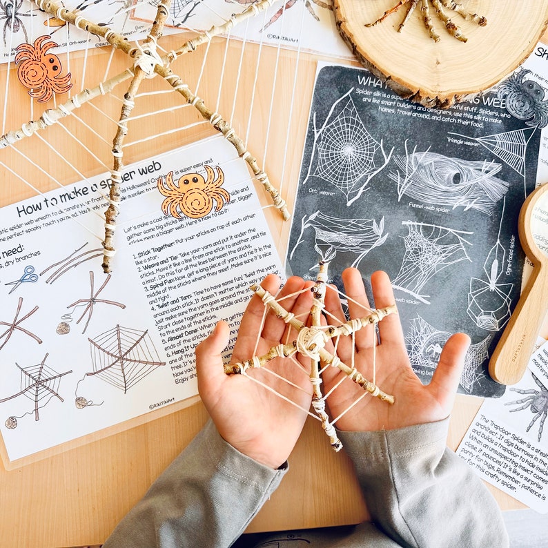 May include: A child's hands hold a spider web craft made with twigs and string. The web is a star shape with a small spider in the center. The image includes instructions for making a spider web craft with twigs and string.