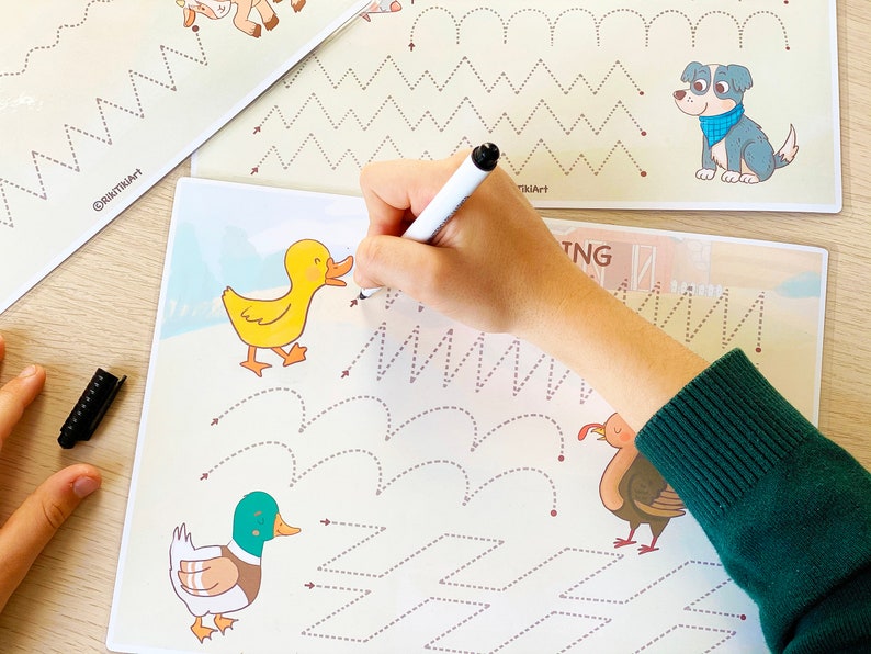 May include: A child's hand traces dotted lines on a white sheet of paper with a black marker. The paper has illustrations of a duck, a goose, and a turkey. The paper also has dotted lines in the shape of zigzags, waves, and squares. The paper has the text "Tracing" at the top.