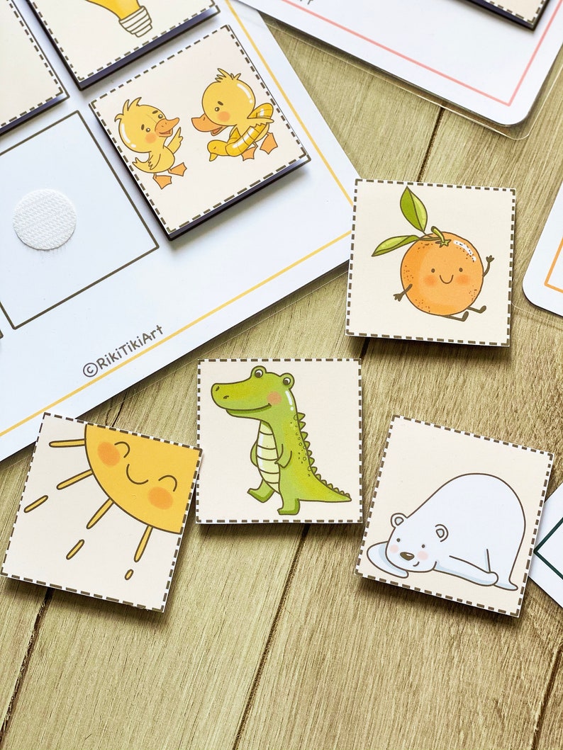 Puede incluir: Un conjunto de tarjetas ilustradas coloridas con una variedad de animales y objetos, incluyendo un sol, un cocodrilo, un oso polar, un pato, una naranja y una bombilla. Las tarjetas est&aacute;n impresas en cartulina blanca y tienen un borde punteado.