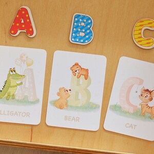 May include: Three colorful alphabet blocks, A, B, and C, with a matching set of flashcards featuring an alligator, bear, and cat. Each card has the letter and the animal's name.