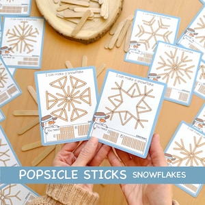 May include: Cards with snowflake designs and the text "I can make a snowflake" are displayed. The cards feature a snowman graphic and instructions for popsicle stick crafts. The words "POPSICLE STICKS SNOWFLAKES" are also visible.