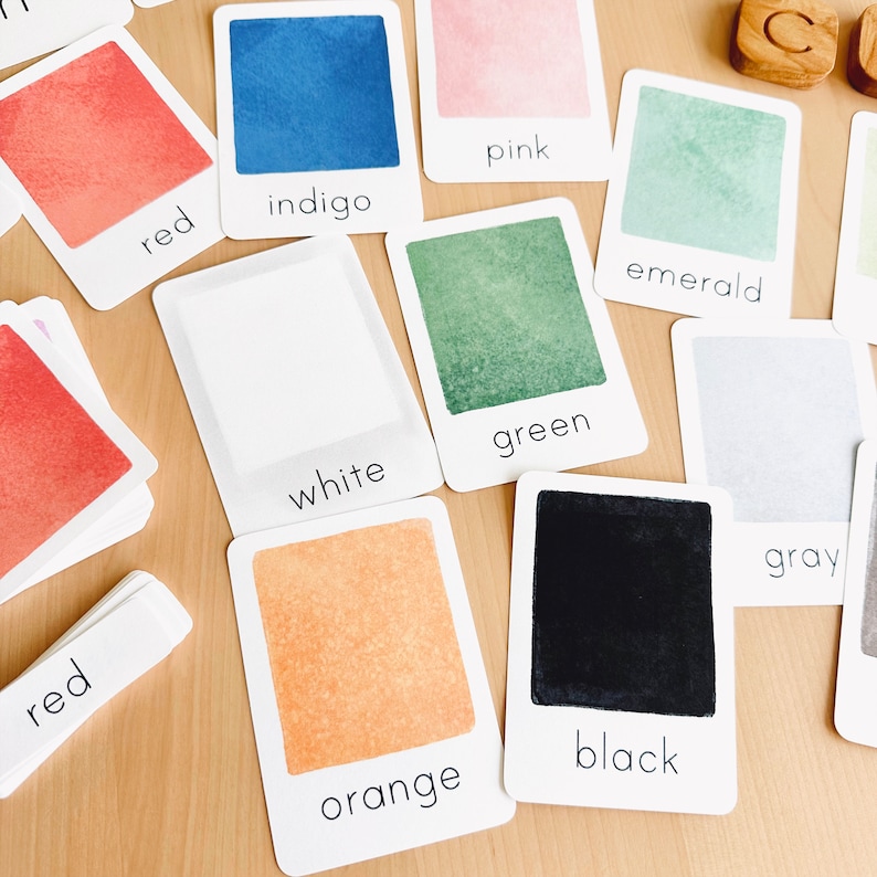 May include: Color recognition cards with watercolor-style backgrounds. The cards feature the words "red", "indigo", "pink", "emerald", "white", "green", "orange", "black", and "gray".