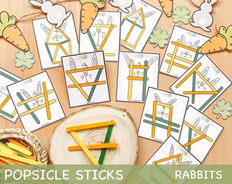 Puede incluir: Un conjunto de tarjetas de actividad imprimibles que presentan contornos de conejos con la palabra "RABBIT" impresa en cada tarjeta. Las tarjetas están diseñadas para usar con palitos de paleta para crear las formas de conejo. La imagen también incluye una pila de palitos de paleta y una guirnalda de zanahorias y conejos.