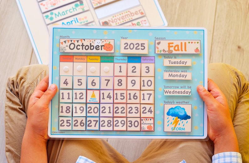 May include: A wooden calendar with a blue frame and a light blue background. The calendar is for October 2025 and shows the days of the week, the date, and the season, which is Fall. The calendar also includes a weather icon for a storm.