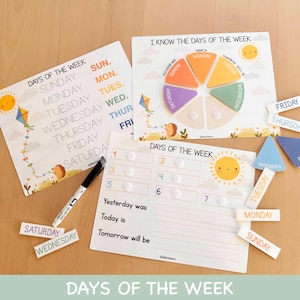 Pode incluir: Conjunto educativo de aprendizagem dos dias da semana. Inclui três quadros brancos com ilustrações coloridas de um sol, uma pipa e um ouriço. O conjunto inclui etiquetas magnéticas de dias e um marcador de quadro branco. O texto "DAYS OF THE WEEK" é visível.