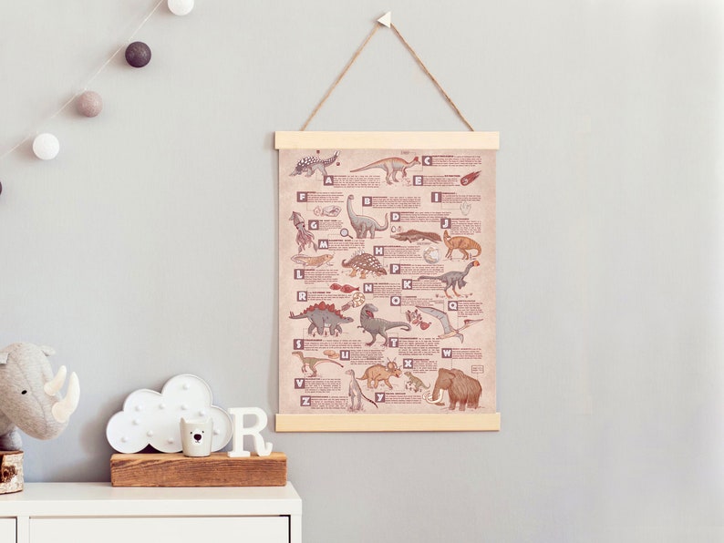 Puede incluir: Un p&oacute;ster de alfabeto ilustrado beige y marr&oacute;n con dinosaurios y otras criaturas prehist&oacute;ricas. El p&oacute;ster est&aacute; enmarcado con un marco de madera claro y est&aacute; colgado en una pared gris claro.