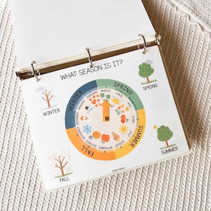 May include: A spiral-bound educational chart titled "WHAT SEASON IS IT?" features a circular design with seasonal illustrations and months. The chart includes images of trees, snowflakes, and fruits, with the seasons labeled: Winter, Spring, Summer, and Fall.
