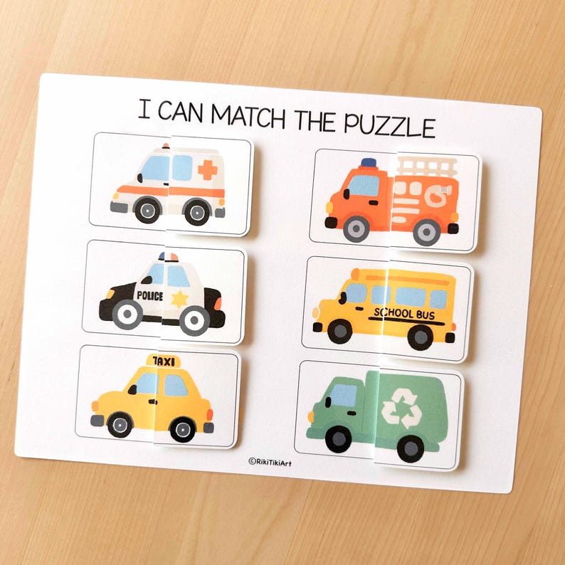 May include: A white puzzle board with the text "I CAN MATCH THE PUZZLE" at the top. The puzzle features six vehicle images: an ambulance, fire truck, police car, school bus, taxi, and a recycling truck. Each vehicle is a separate puzzle piece.