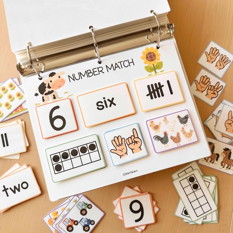 May include: A white binder with the words "NUMBER MATCH" and matching number cards. The cards feature numbers, number words, tally marks, and visual representations like fingers, farm animals, and a ten-frame. Educational learning tool.