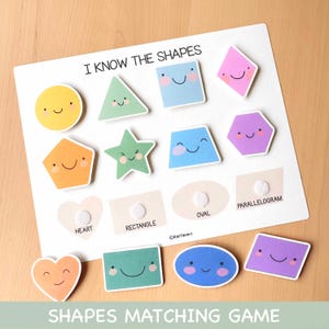 Op de afbeelding: Een wit bordspel met de tekst "I KNOW THE SHAPES" en "SHAPES MATCHING GAME". Het spel bevat kleurrijke, lachende vormuitsparingen, waaronder een cirkel, een driehoek, een vierkant en een ster. De vormen zijn geel, groen, blauw, oranje, roze en paars.