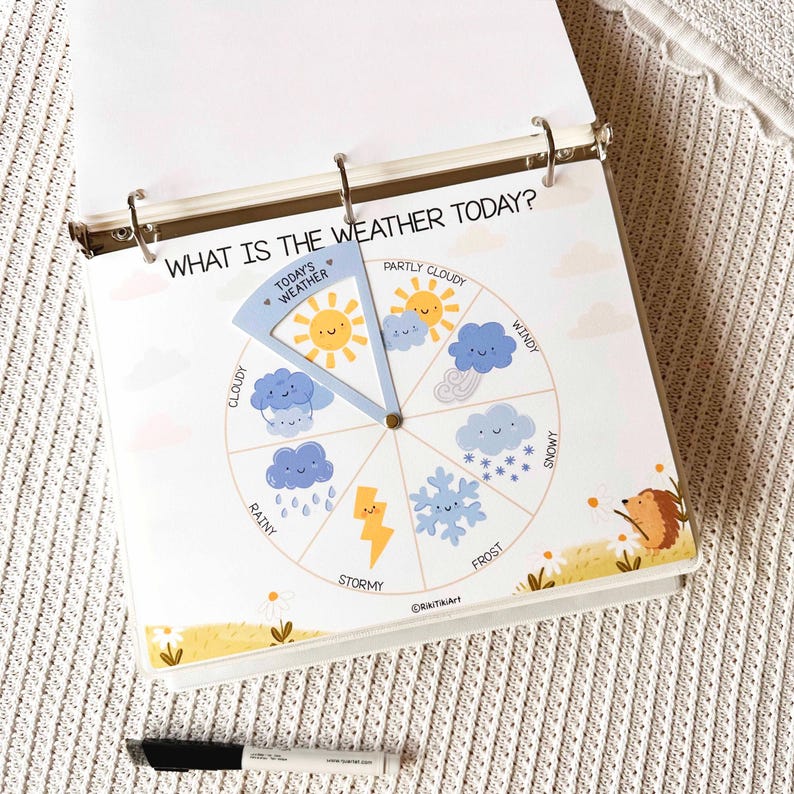 May include: A children's weather chart in a binder. The chart features a rotating wheel with illustrations of different weather conditions, including sunny, cloudy, rainy, and snowy. Text reads "WHAT IS THE WEATHER TODAY?" and "TODAY'S WEATHER".