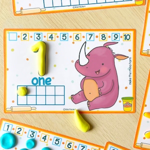 May include: A printable learning card with a rhino illustration and the number one written in yellow playdough. The card has a grid with a single yellow playdough circle in the first square. The text "one" is written below the grid. The card also includes the numbers 2 through 10 and the text "make the rhino horn".