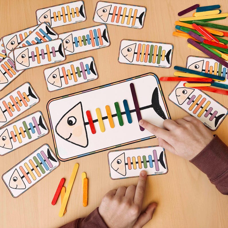 May include: A child's educational game featuring colourful wooden sticks and fish-shaped cards with rainbow-coloured stripes. The game teaches counting and colour recognition.
