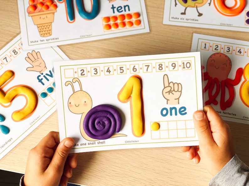 May include: A printable learning activity for children featuring a snail with a purple shell, a yellow number one, and the word "one" written in blue. The activity includes a grid for counting and a number line with numbers 1 through 10.