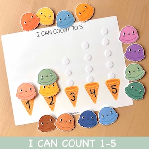 Puede incluir: Un juego educativo para niños con bolas y conos de helado. La pizarra blanca tiene el texto "I CAN COUNT TO 5" y los números 1-5. Las bolas de helado son de varios colores, incluyendo naranja, amarillo, azul y verde.
