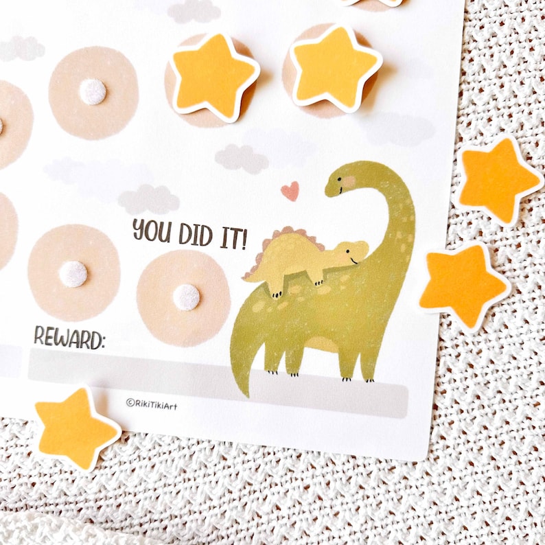 May include: A reward chart with a dinosaur theme. The chart features a large green dinosaur with a smaller yellow dinosaur on its back, along with star-shaped stickers. Text on the chart reads "YOU DID IT!" and "REWARD:"