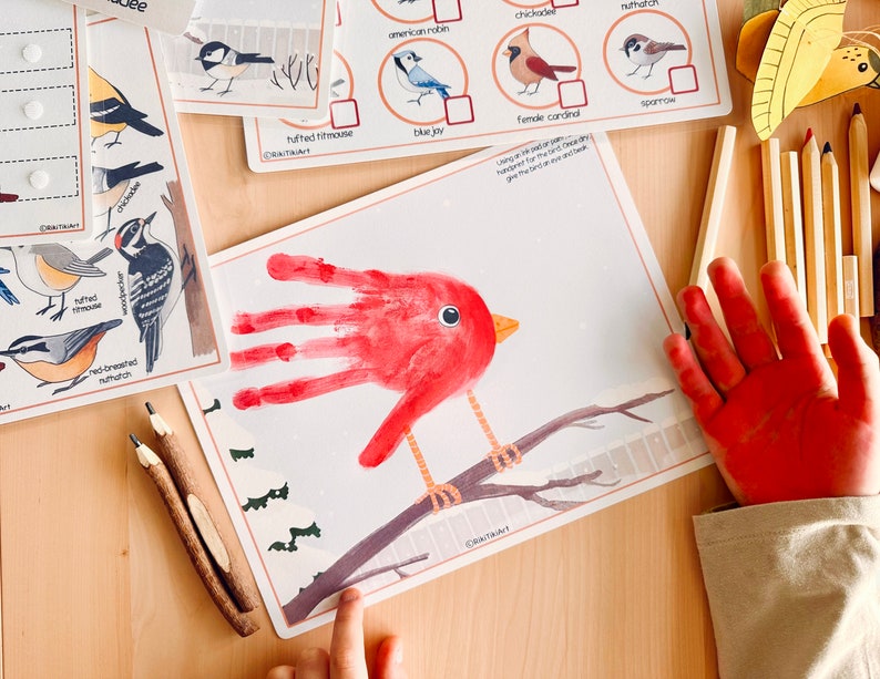 May include: A red handprint is used to create a cardinal bird on a branch with green trees in the background. The image includes a printable worksheet with a variety of bird illustrations and names.