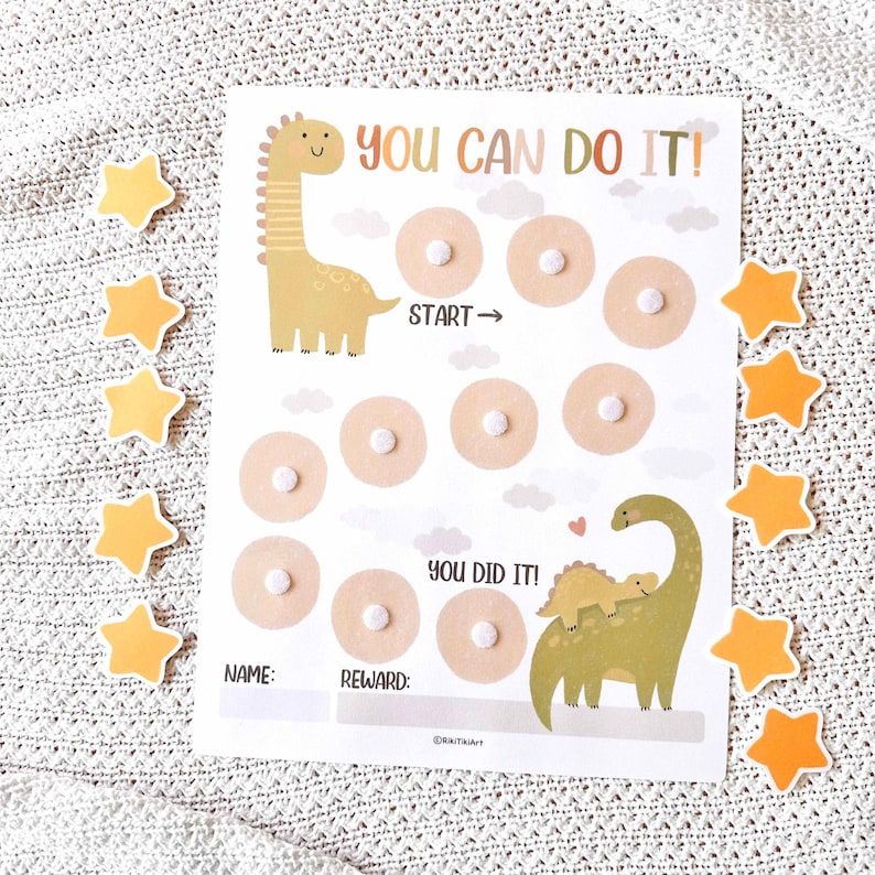 May include: A reward chart with the text "YOU CAN DO IT!" and "YOU DID IT!" featuring dinosaur illustrations. The chart has spaces for rewards and is surrounded by star-shaped stickers. The chart is on a white background.