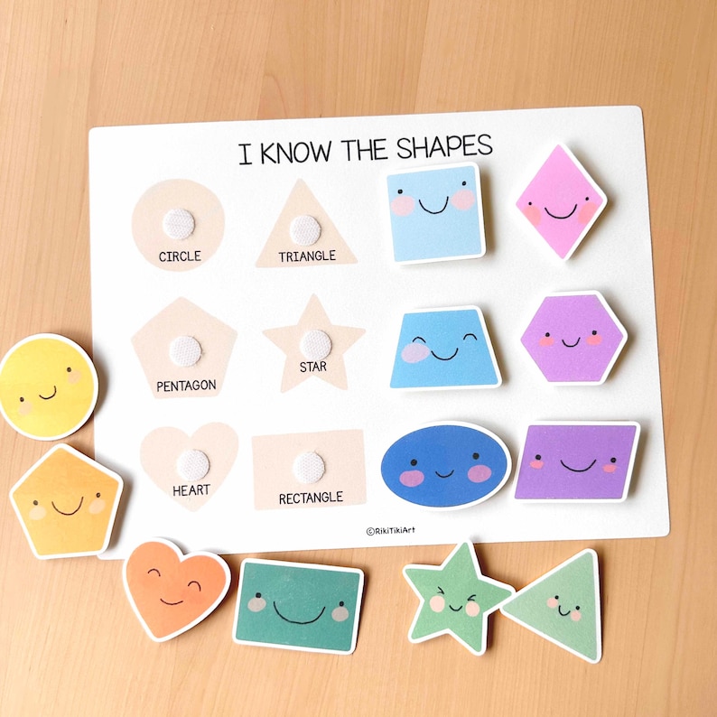 Pu&ograve; includere: Un giocattolo educativo in legno bianco con la scritta "I KNOW THE SHAPES". Il giocattolo presenta vari ritagli di forme colorate e sorridenti, tra cui cerchi, triangoli e stelle. Le forme sono progettate per essere posizionate sulla lavagna, promuovendo il riconoscimento delle forme.