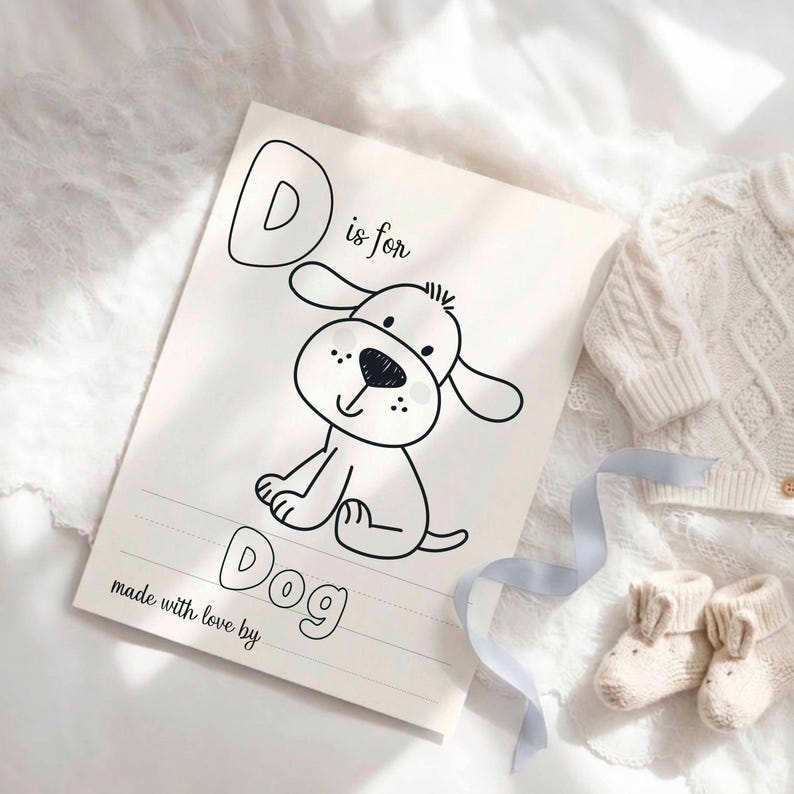 May include: A white rectangular card featuring a black line drawing of a puppy. The text reads D is for Dog and made with love by. The card includes dashed lines for writing practice, positioned next to a pair of small cream-colored knit baby booties.