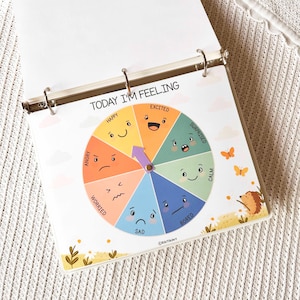 May include: A colorful emotion wheel titled "TODAY I'M FEELING" with sections for Happy, Excited, Surprised, Calm, Bored, Sad, Angry, and Worried. A purple arrow points to an emotion. The wheel is in a binder.