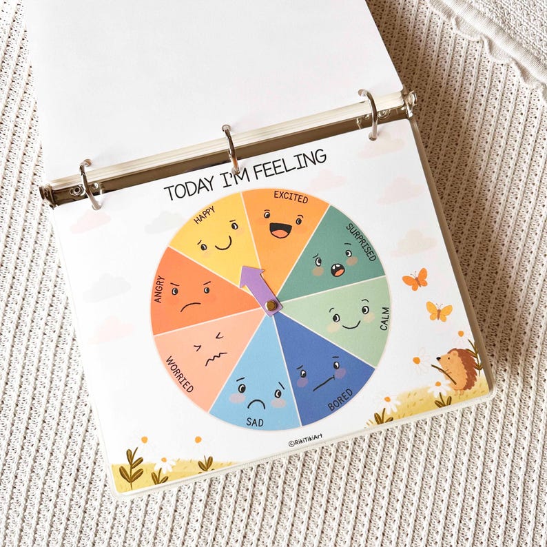 May include: A colorful emotion wheel titled "TODAY I'M FEELING" with sections for Happy, Excited, Surprised, Calm, Bored, Sad, Angry, and Worried. A purple arrow points to an emotion. The wheel is in a binder.