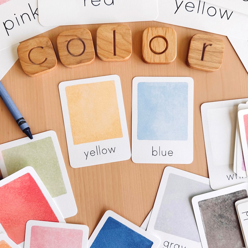 May include: Wooden letter tiles spelling out the word "color" with color swatches in yellow, blue, green, red, pink, and gray. The swatches are on cards with the color name printed below.